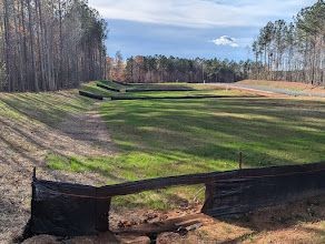 Grassy area with black silt fences and forest in the background under a cloudy sky.