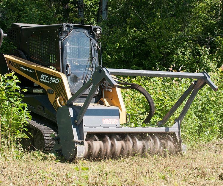 Forestry bulldozer clearing vegetation in a forested area during daytime.